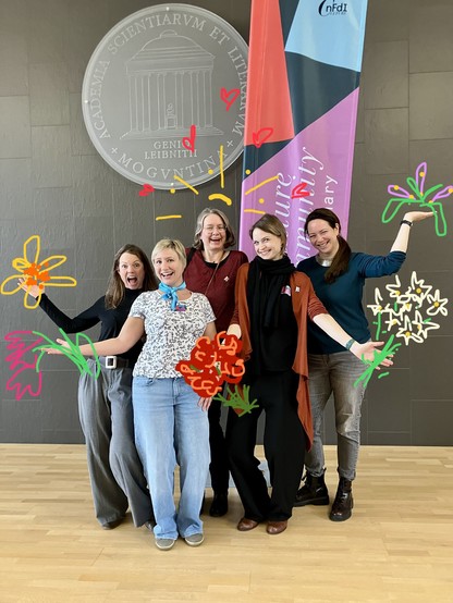 Das Social Media-Team von NFDI4Culture posiert mit ausgestreckten Armen auf der Bühne des Plenarsaals der Akademie der Wissenschaften und Literatur. Drumherum sind Blumenfilter und Grafikelemente ergänzt worden.